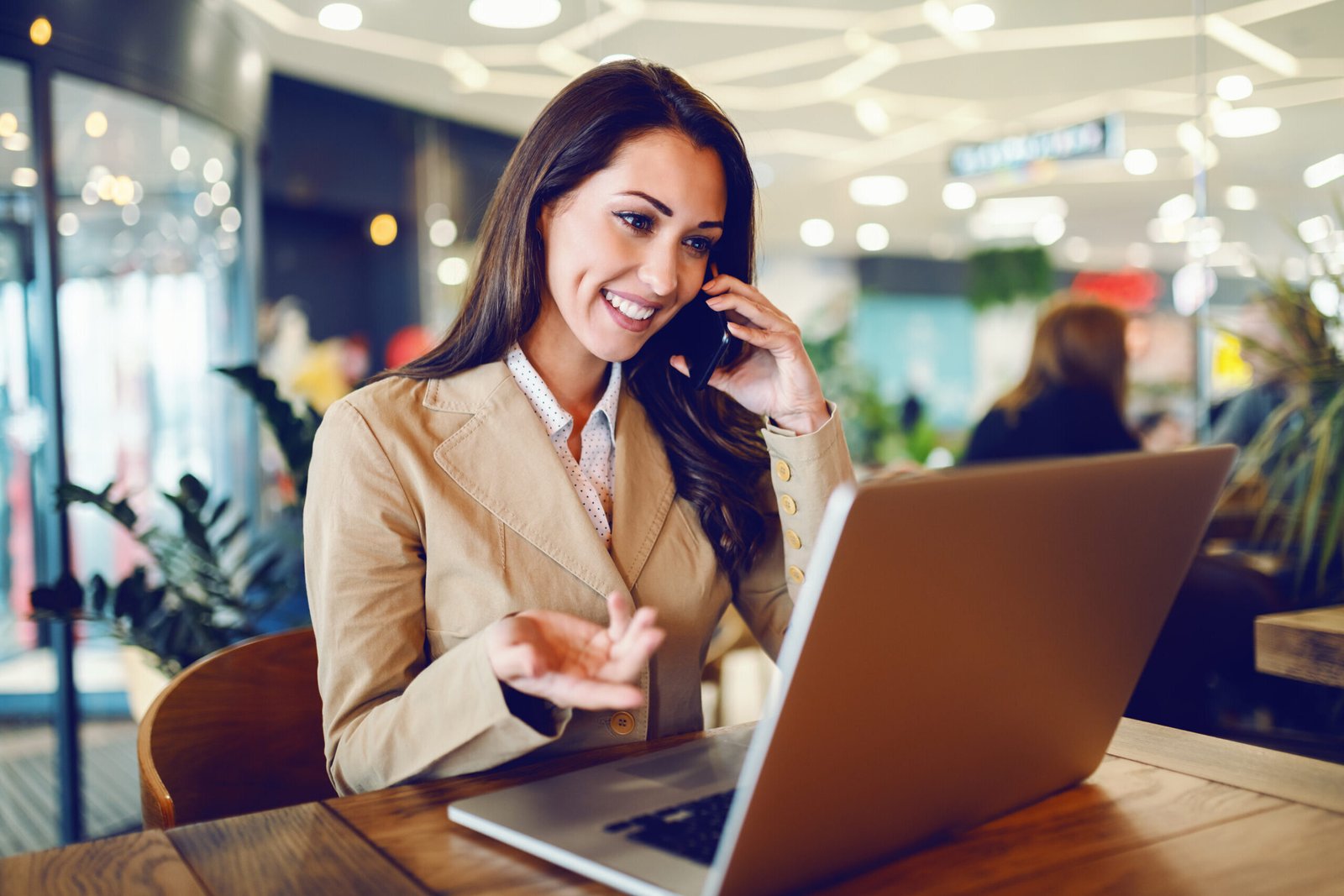 Attractive businesswoman in beige jacket sitting in cafe, talkin